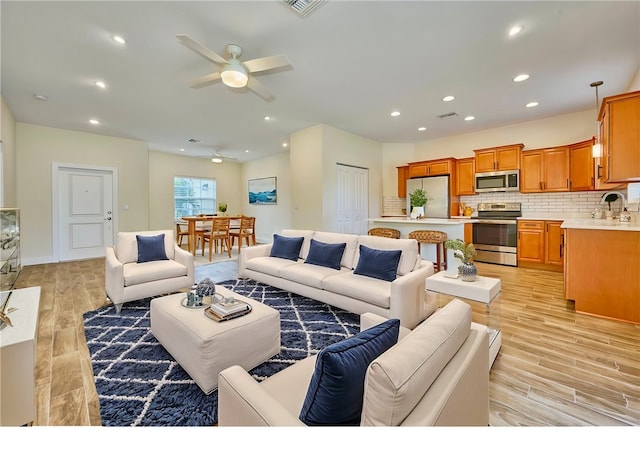 living room featuring ceiling fan, sink, and light wood-type flooring