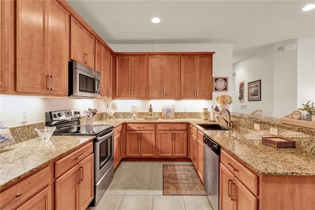 kitchen with light stone countertops, appliances with stainless steel finishes, kitchen peninsula, and sink