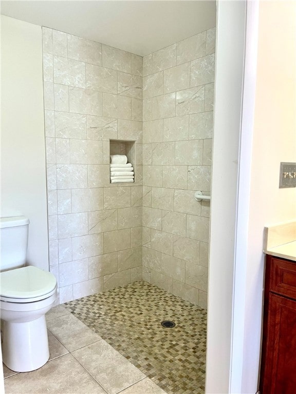 bathroom featuring tile patterned flooring, tiled shower, toilet, and vanity