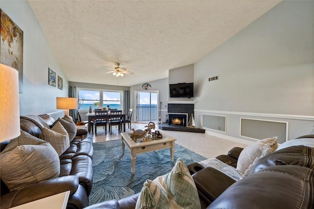 living room featuring light tile patterned flooring, ceiling fan, lofted ceiling, and a textured ceiling