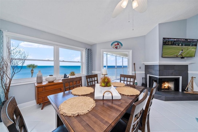 dining space with vaulted ceiling, light tile patterned flooring, a water view, and a fireplace