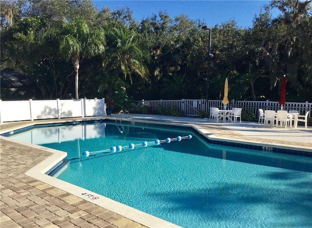 community pool featuring outdoor dining area, a patio, and fence