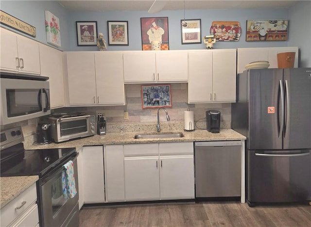 kitchen with a sink, stainless steel appliances, a toaster, white cabinetry, and backsplash