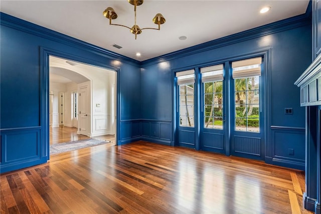 121 Palm Island Ln, Vero Beach, FL 32963 - unfurnished room with a decorative wall, arched walkways, ornamental molding, a chandelier, and wood finished floors