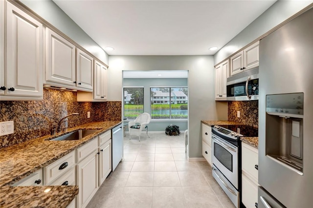 kitchen featuring dark stone counters, sink, light tile patterned floors, white cabinetry, and stainless steel appliances