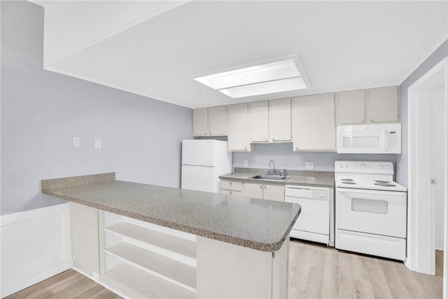 kitchen featuring white appliances, a peninsula, a sink, and light wood-style floors