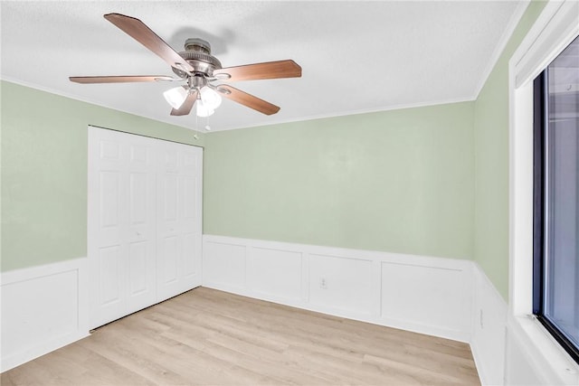 empty room with crown molding, ceiling fan, light wood-style flooring, and a wainscoted wall
