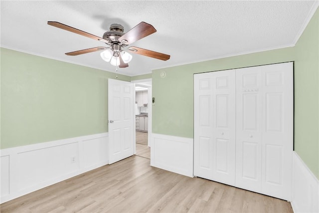 unfurnished bedroom with a textured ceiling, crown molding, wood finished floors, a wainscoted wall, and a closet