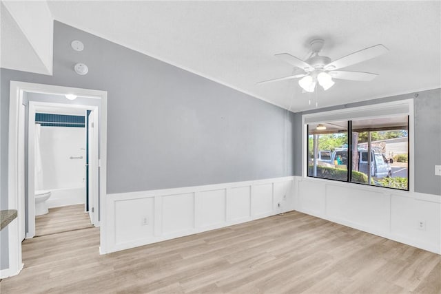 spare room with a decorative wall, ceiling fan, a wainscoted wall, and light wood-type flooring