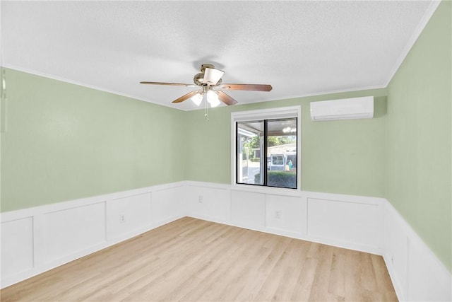 spare room featuring ceiling fan, an AC wall unit, a textured ceiling, light wood-type flooring, and ornamental molding