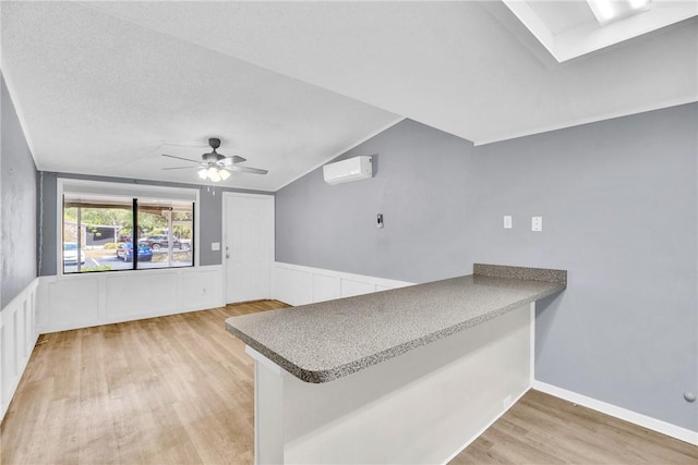 kitchen with ceiling fan, a wall mounted AC, a peninsula, light wood finished floors, and lofted ceiling