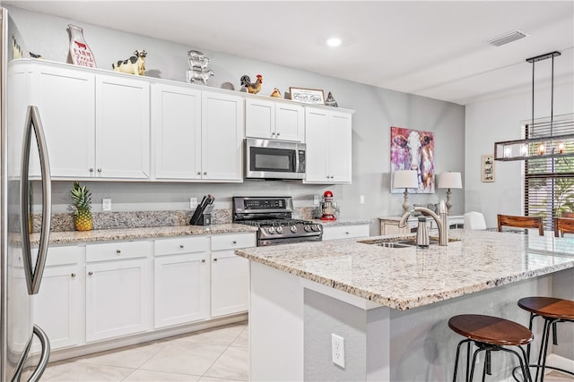 kitchen featuring stainless steel appliances, decorative light fixtures, sink, an island with sink, and white cabinets