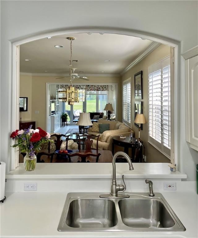 kitchen with pendant lighting, sink, ornamental molding, and white cabinets