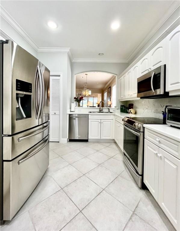 kitchen with appliances with stainless steel finishes, white cabinetry, sink, light tile patterned floors, and crown molding