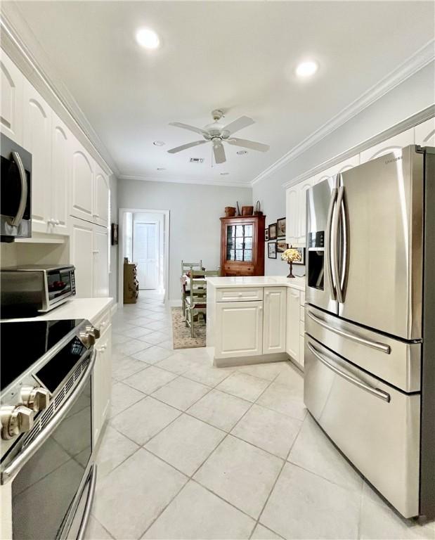 kitchen featuring appliances with stainless steel finishes, white cabinetry, ornamental molding, light tile patterned flooring, and kitchen peninsula