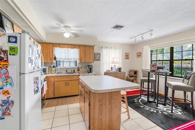 kitchen with light tile patterned floors, plenty of natural light, a center island, and white fridge