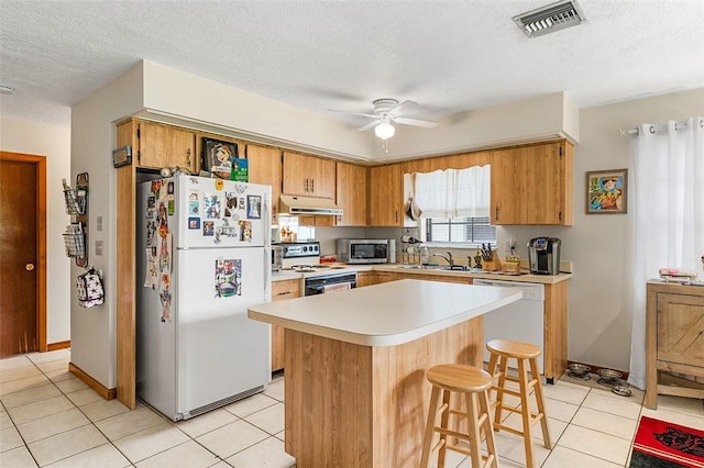 kitchen with light tile patterned floors, white appliances, ceiling fan, a center island, and a textured ceiling