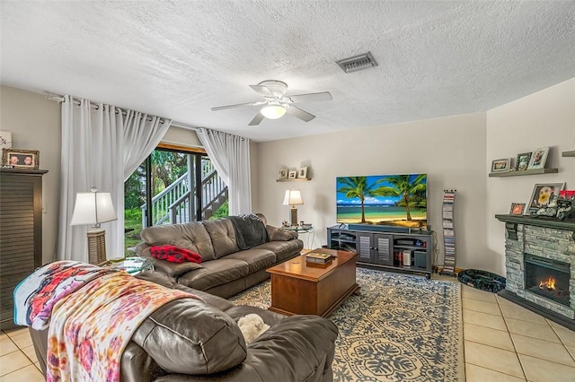 living room with light tile patterned floors, a stone fireplace, a textured ceiling, and ceiling fan