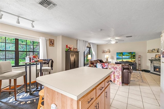 kitchen featuring a fireplace, light brown cabinetry, a center island, light tile patterned floors, and ceiling fan