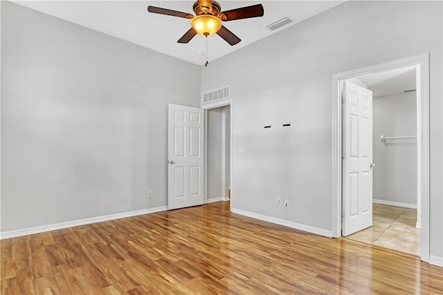 unfurnished bedroom with light wood-type flooring, a walk in closet, ceiling fan, and a towering ceiling