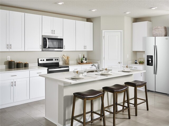 kitchen featuring a center island with sink, stainless steel appliances, white cabinetry, a textured ceiling, and sink