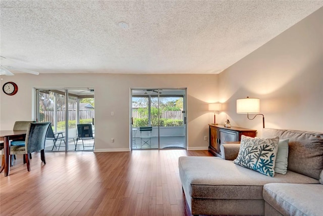 living room with a ceiling fan, a textured ceiling, baseboards, and wood finished floors