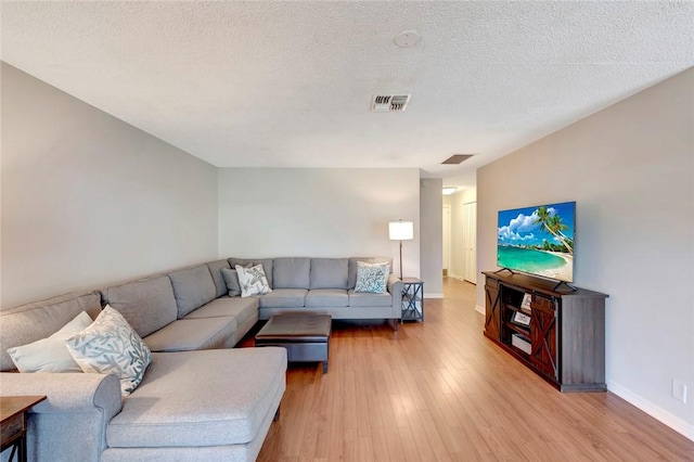 living area with a textured ceiling, light wood finished floors, visible vents, and baseboards