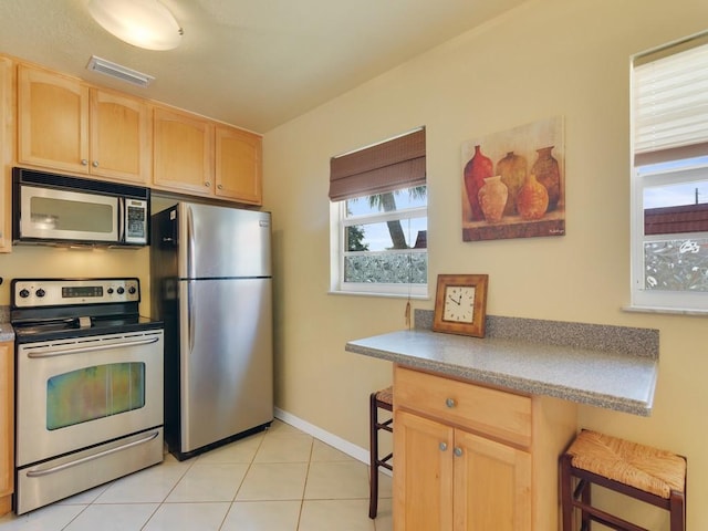 kitchen with light brown cabinetry, light tile patterned floors, a breakfast bar, and appliances with stainless steel finishes