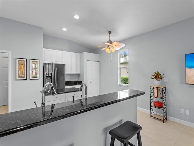 kitchen featuring stainless steel refrigerator with ice dispenser, dark stone countertops, ceiling fan, white cabinets, and vaulted ceiling