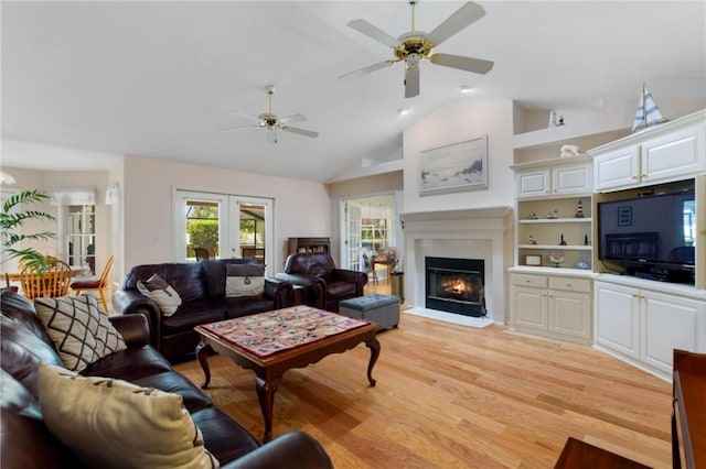 living room with a ceiling fan, light wood finished floors, a fireplace with flush hearth, lofted ceiling, and french doors