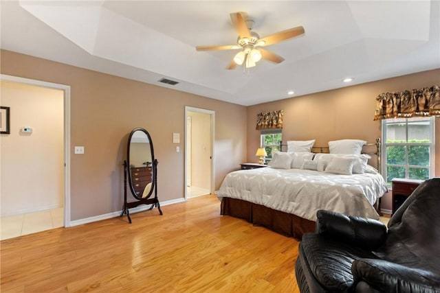 bedroom with a tray ceiling, light wood-style floors, recessed lighting, baseboards, and a ceiling fan