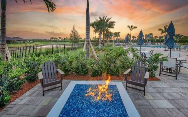 patio terrace at dusk featuring a community pool, an outdoor fire pit, and fence