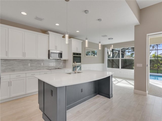 kitchen with a kitchen island with sink, sink, decorative light fixtures, white cabinetry, and stainless steel appliances