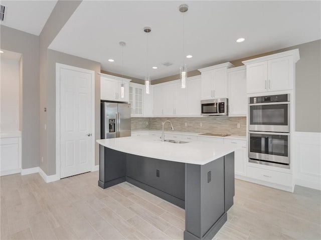 kitchen featuring appliances with stainless steel finishes, a kitchen island with sink, sink, pendant lighting, and white cabinetry