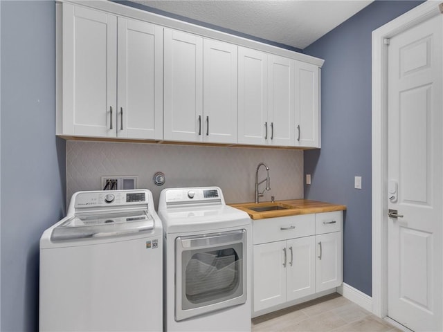 clothes washing area with sink, cabinets, a textured ceiling, light tile patterned floors, and washer and dryer