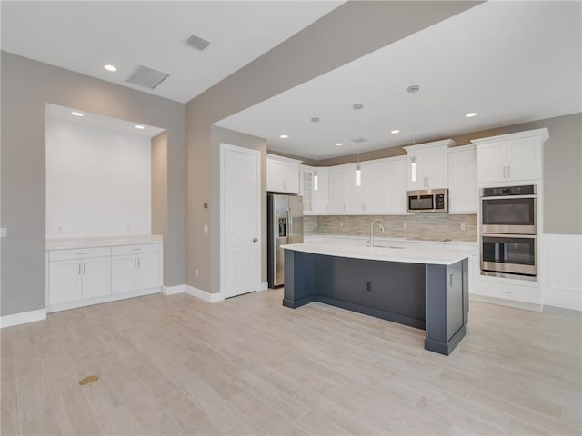 kitchen featuring white cabinets, appliances with stainless steel finishes, pendant lighting, and an island with sink