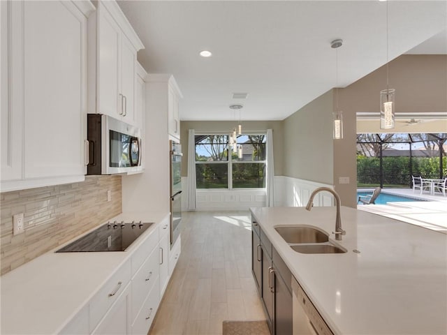 kitchen featuring stainless steel appliances, sink, light hardwood / wood-style flooring, white cabinets, and hanging light fixtures