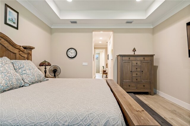 bedroom with wood-type flooring, a raised ceiling, and ornamental molding