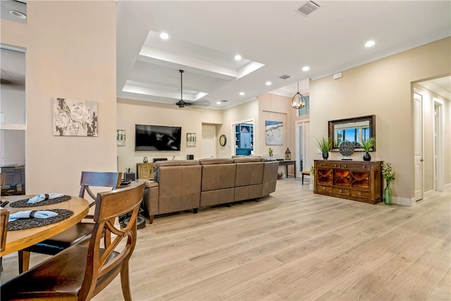 living room featuring ceiling fan with notable chandelier, light wood-type flooring, and a tray ceiling