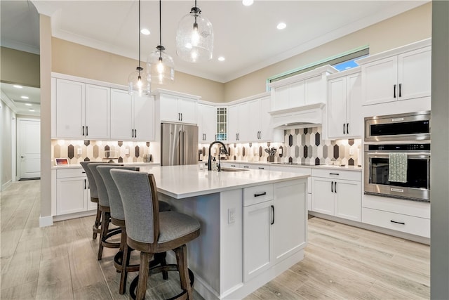 kitchen featuring a kitchen island with sink, high end refrigerator, white cabinets, light hardwood / wood-style flooring, and decorative light fixtures