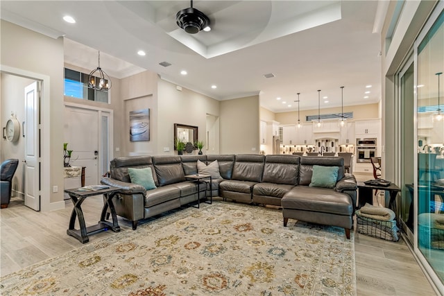 living room featuring ceiling fan with notable chandelier, light wood-type flooring, and crown molding