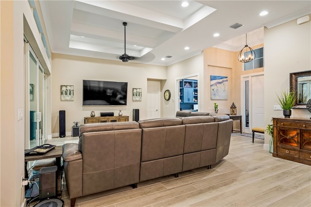 living room with ceiling fan with notable chandelier, a raised ceiling, and light wood-type flooring