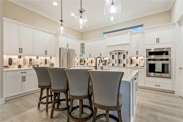 kitchen with white cabinets, pendant lighting, high quality fridge, and an island with sink