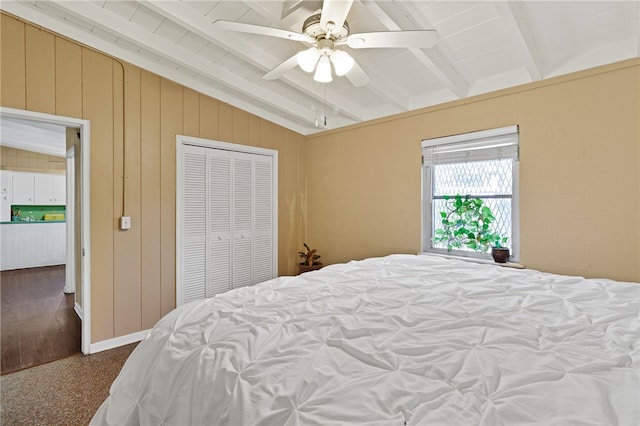 bedroom with ceiling fan, wood walls, a closet, and vaulted ceiling with beams