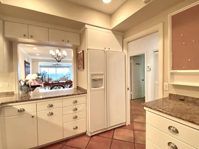 kitchen with white refrigerator with ice dispenser, pendant lighting, a notable chandelier, white cabinetry, and light tile patterned flooring