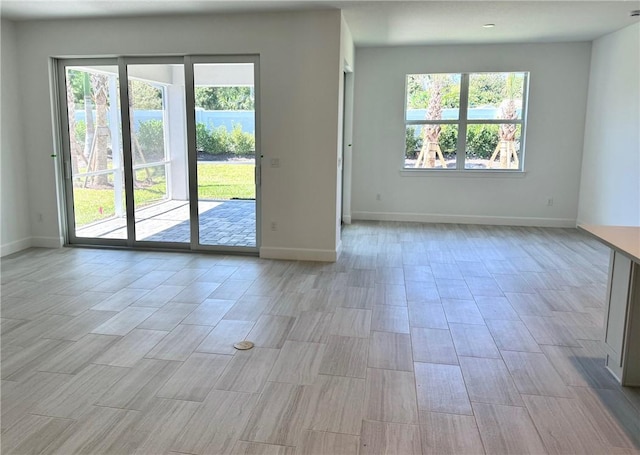 empty room with a wealth of natural light, light wood finished floors, and baseboards