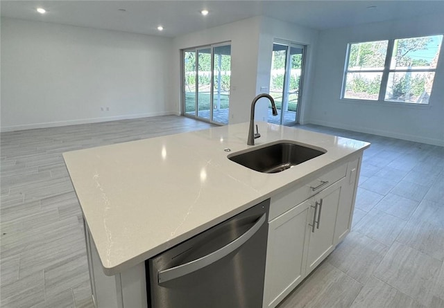 kitchen featuring a kitchen island with sink, a sink, white cabinets, dishwasher, and open floor plan