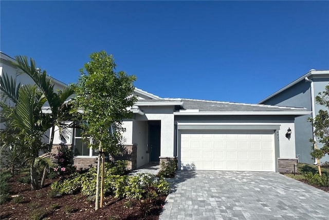 view of front of home with decorative driveway, an attached garage, stone siding, and stucco siding