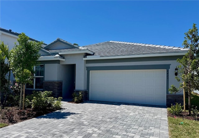 view of front of home featuring an attached garage, stone siding, decorative driveway, and stucco siding