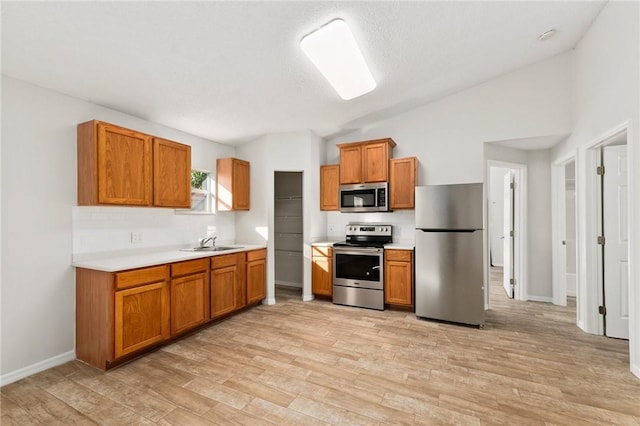 kitchen with sink, light wood-type flooring, stainless steel appliances, and vaulted ceiling